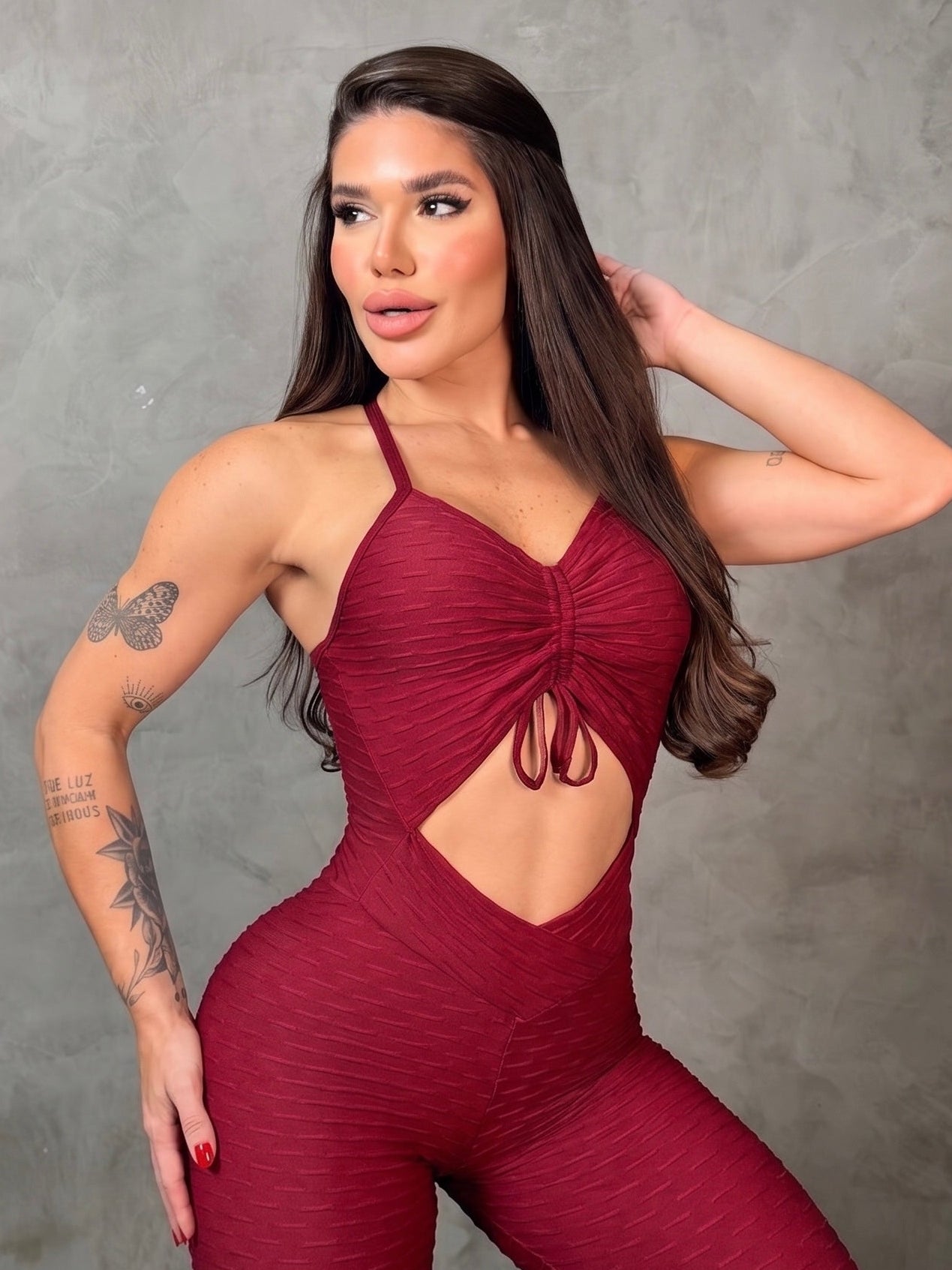 Woman wearing a maroon jumpsuit with cut-out design against a gray background